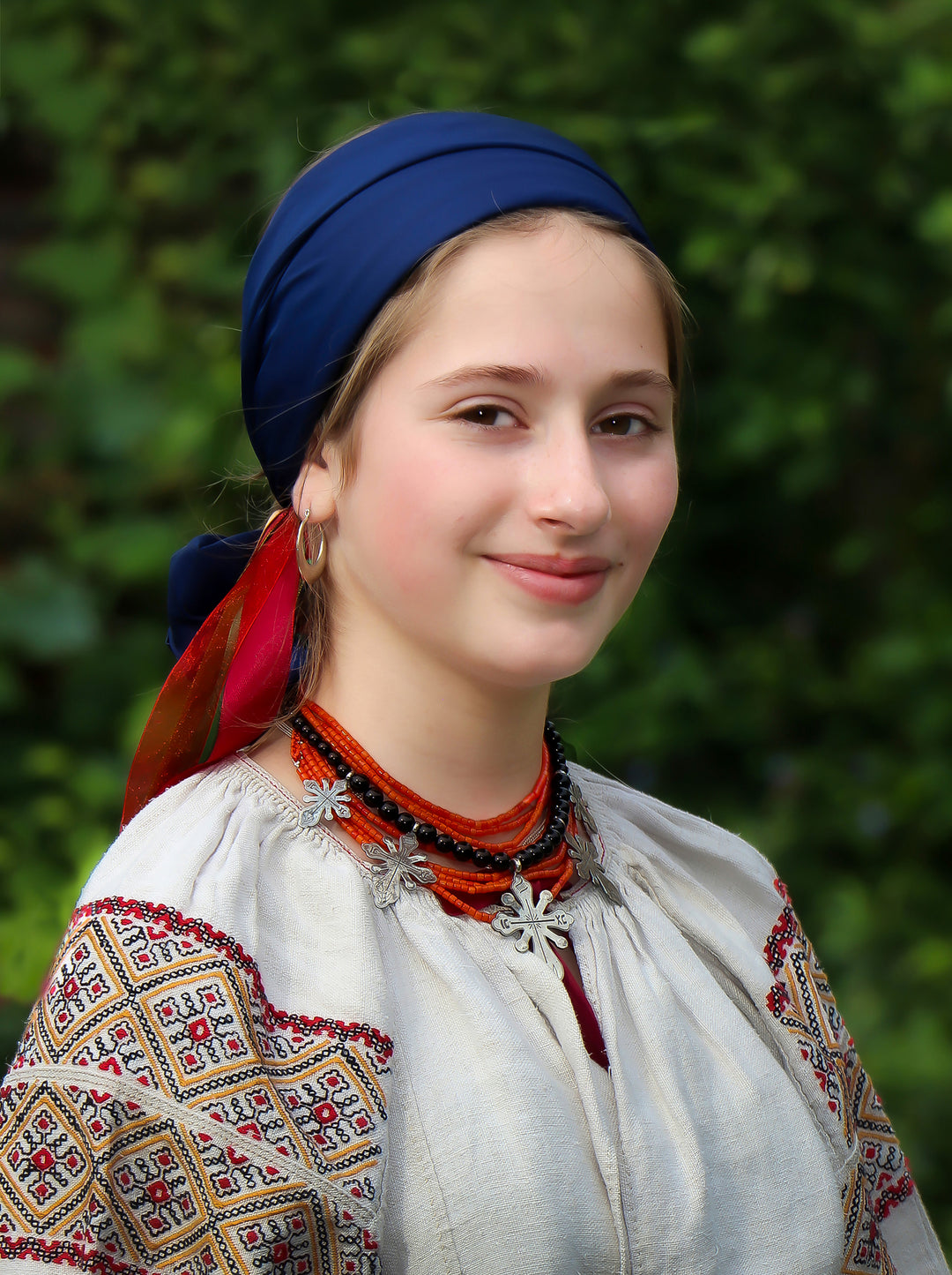 Woman wearing traditional embroidered clothing with a blue headscarf against a green background. Photographer: Ольга Луканіна